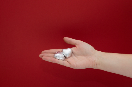 Chocolate heart shaped sweets in the foil laying on a female hand on red background. Beautiful charity and healtcare concept.の写真素材