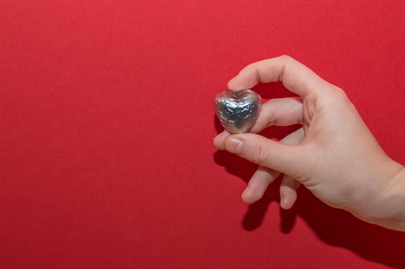 Chocolate heart shaped sweet holding by female hand on red background. Beautiful charity and healtcare concept.の写真素材