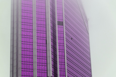 Futuristic photography of the facade of the skyscraper with ultra violet windows standing in the fogの写真素材