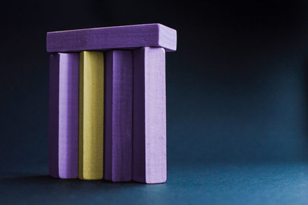 Yellow wood bar besieged with violet wood bars on the dark blue background. Concept of the racism, sexual discrimination, domination, social problems, emotional stress.の写真素材