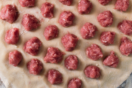 Meat balls laying on the rolled out wheat dough. Dumplings cooking.の写真素材