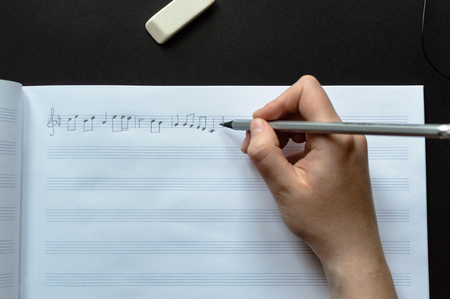 Top view of the female's hand writing music notes in the blank music sheets. Concept of the education in arts, music, creativity, music notes writing.の写真素材