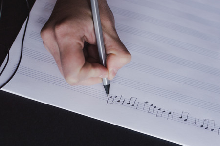 Close-up view of the hand writing music notes with the pencil in the blank music sheets. Concept of the education in arts, music, creativity, music notes writing.の写真素材