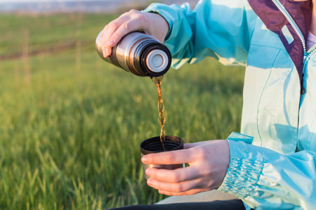 Young traveller filling the tourists cup with tea from the old vacuum flask. Concept of the travelling, backpacking, hiking, outdoor recreation, success, inspiration,の写真素材