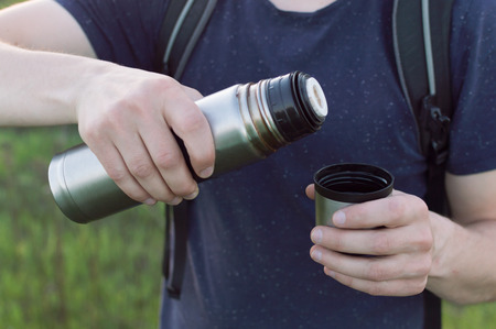 Young male traveller filling the travelling cup with the tea from the vacuum bottle. Concept of the travelling, backpacking, hiking, outdoor recreation, success, inspiration.の写真素材