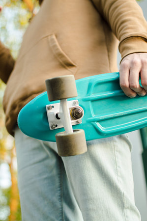 Side view of the young man holding his blue plastic penny board . The concept of modern culture, penny skateboarding, outdoor activity, modern lifestyle.の写真素材