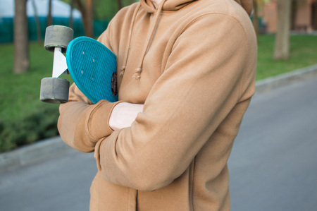 Side view of the young man holding his blue plastic penny board . The concept of modern culture, penny skateboarding, outdoor activity, modern lifestyle.の写真素材