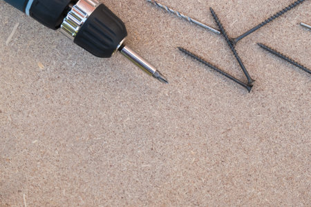 Electric screwdriver with black long srews laying on the brown wooden board. Background with copy...