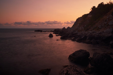 Long exposure photography of the sea waves splashing near to the clif when the sun is going down.