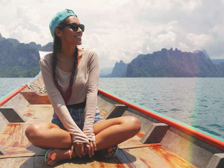 Young Happy Mixed Race Girl Sitting and Relaxing on Traditional Thai Wooden Long Tail Boat at Khao Sok Lake. Phang Nga Province, Thailand.の写真素材