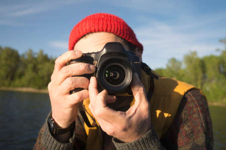 Closeup Portrait of a Man Taking a Picture with Professional Photo Camera on a Lake.の写真素材
