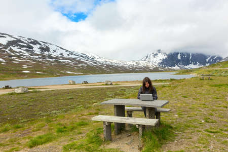 Young girl working on a laptop among mountainsの写真素材
