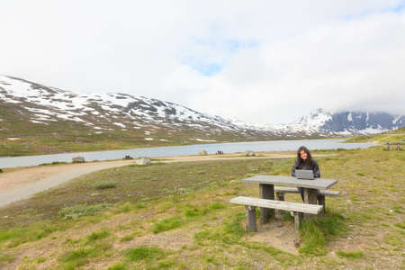 Young girl working on laptop among mountainsの写真素材
