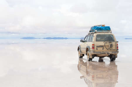Car moving on the reflected surface of Salar de Uyuni lake in Boliviaの写真素材