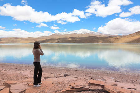 Woman talking on the mobile phone at the shore of lagoon Celeste, Boliviaの写真素材