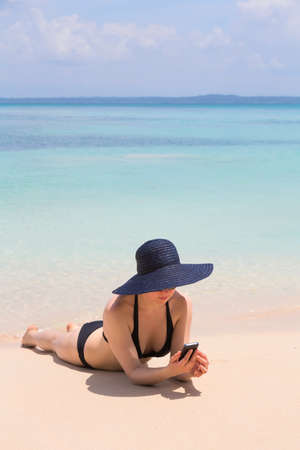 Woman looking at mobile phone on the beach, archipelago Bocas del Toro, Panamaの写真素材