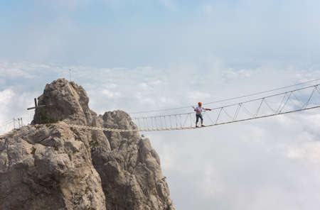 Man crossing the chasm on the hanging bridge (focus on the man)の写真素材