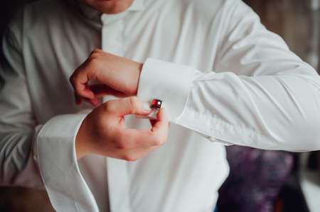 Groom buttoning a shirt on a white weddingの写真素材