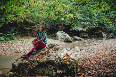girl tourist sits on a rock in the woods background of mountain riverの写真素材