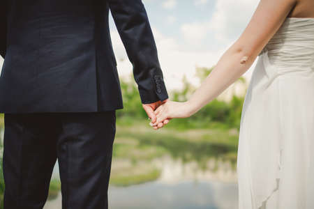 groom holds his brides hand on a background of lakeの写真素材