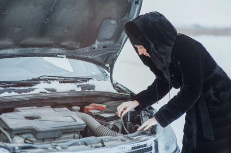 girl looks under cowl of broken car on rural road