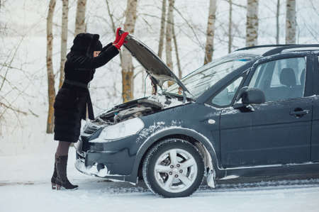 girl looks under cowl of broken car on rural roadの写真素材