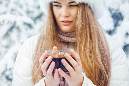 Beautiful girl with a cup of tea in his hands in the winter forest. Close-upの写真素材