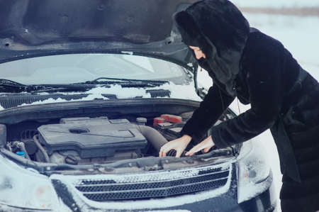 Young redhead girl looks under cowl of broken car on rural roadの写真素材