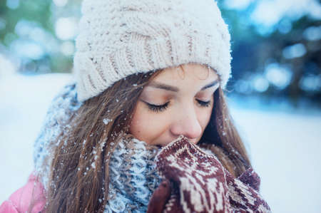 The girl warms hands in mittens in winter forest. Snow on eyelashesの写真素材