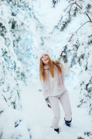Beautiful young girl posing in the winter in cold snowy forest with pine trees.の写真素材