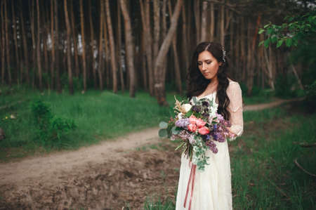Beautiful bride in the forest with a large bouquet of different flowers. Boho styleの写真素材