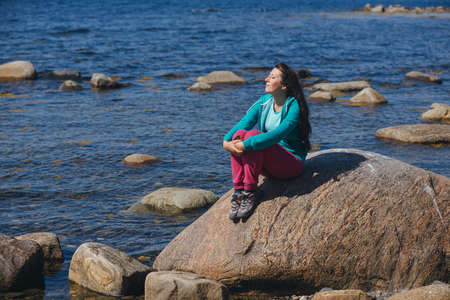 Tourist girl sitting on a rock against the seaの写真素材