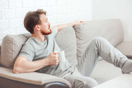 bearded man sitting at home on the sofa with a cup of teaの写真素材