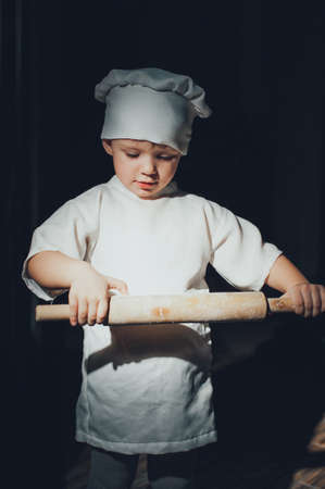 Baby cook with a rolling pin on a black backgroundの写真素材