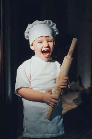 Baby cook with a rolling pin on a black backgroundの写真素材