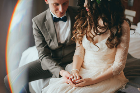 Wedding shot of stylish bride and groom sitting on bed