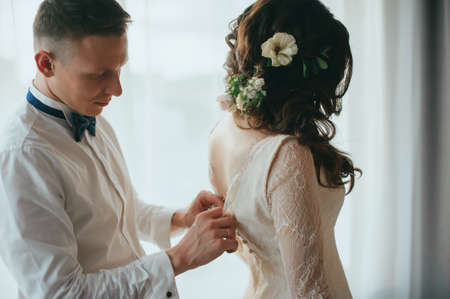 The groom dresses the bride. Wedding preparationsの写真素材