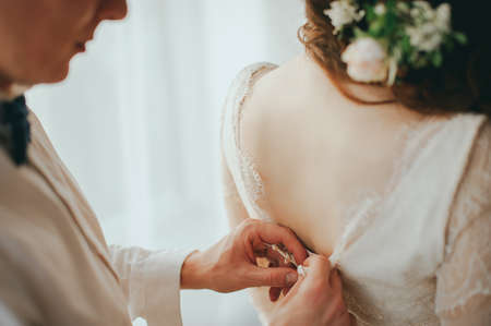 The groom dresses the bride. Wedding preparationsの写真素材