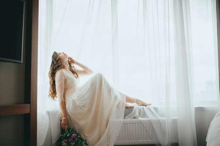 The bride posing against the window. Flying dressの写真素材