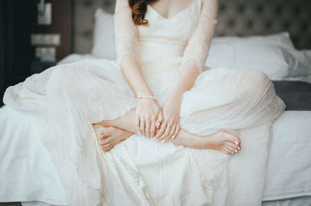 wedding Happy beautiful brunette bride in luxurious wedding dress sitting on bed waiting for groomの写真素材
