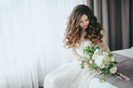 Beautiful stylish bride with bouquet on bedの写真素材
