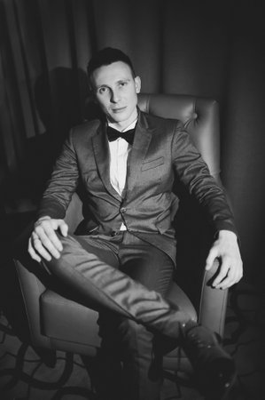Stylish bridegroom in gray suit and butterfly posing in hotel