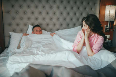 Fashion photo of two young beautiful lovers relax at the hotel on a bed,they are smilingの写真素材