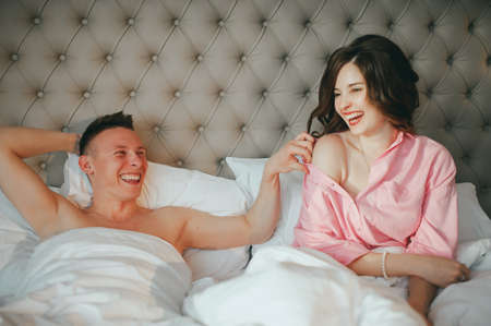 Fashion photo of two young beautiful lovers relax at the hotel on a bed,they are smilingの写真素材
