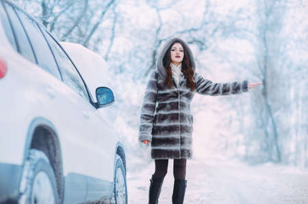 Girl on winter road with the car asking for help.の写真素材