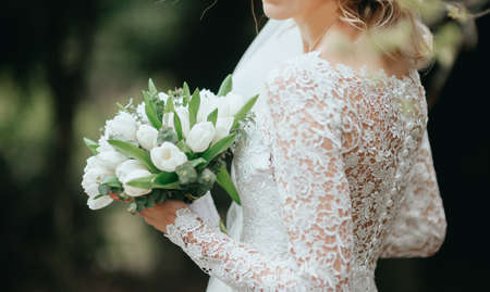 beautiful bouquet of different colors in the hands of the bride in a white dressの写真素材