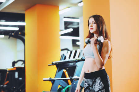 Young beautiful girl is engaged in sports training with dumbbells in the gymの写真素材