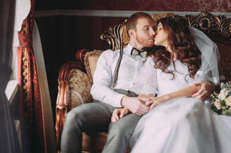 luxury bride in vintage dress with bouquet and stylish groom embracing and smiling at window in morning light in hotel room. happy wedding couple, sensual romantic moment,の写真素材