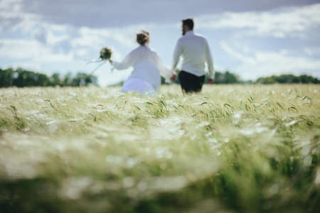 Married couple running in a field, having fun and smiling. She is looking back.の写真素材