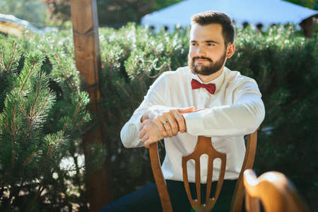 handsome groom with beard posing on a chairの写真素材
